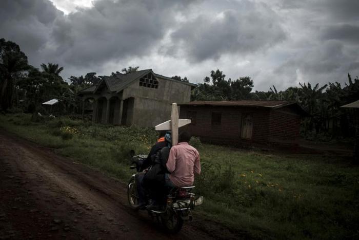 Toll: Three people on a motorbike carry a cross for a grave in Ebola-hit North Kivu