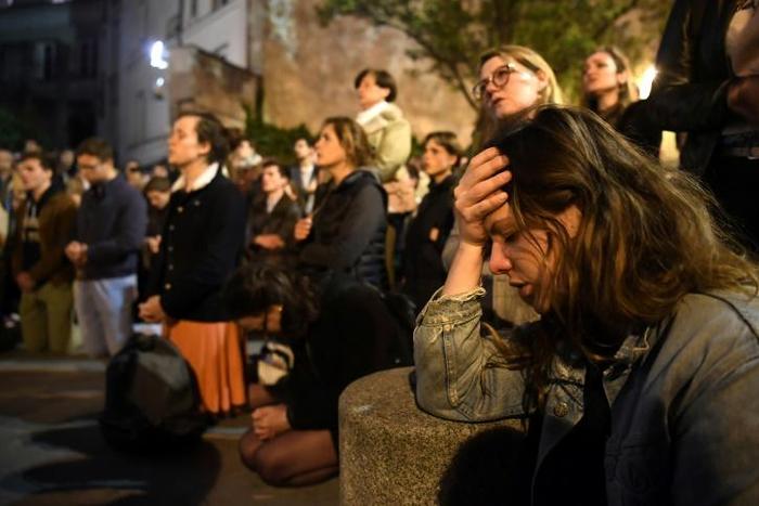 Onlookers react as they watch flames engulf Notre-Dame Cathedral in Paris on April 15, 2019