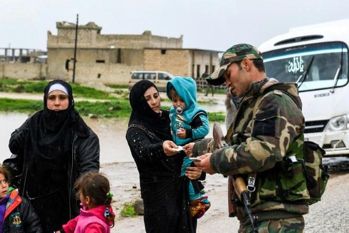A Syrian soldier checks the identification documents of a woman crossing from rebel-held areas in Idlib province into regime-held territories