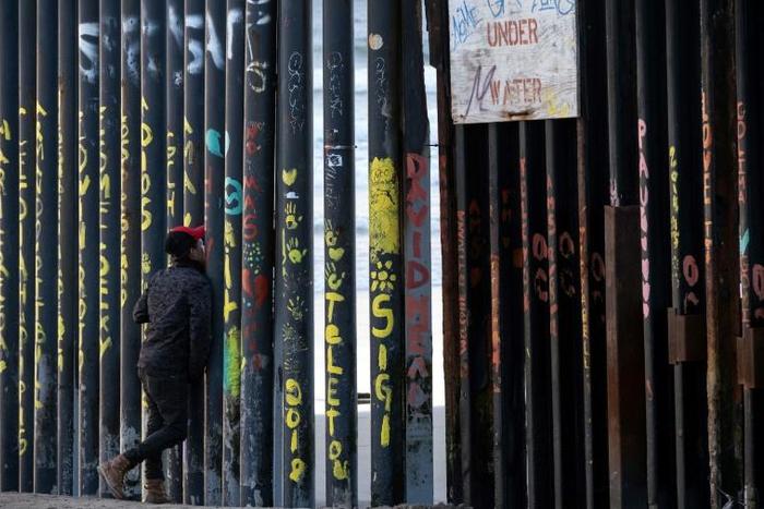A man looks through the US-Mexico border fence in Playas de Tijuana, Baja California State, Mexico, on March 8, 2019