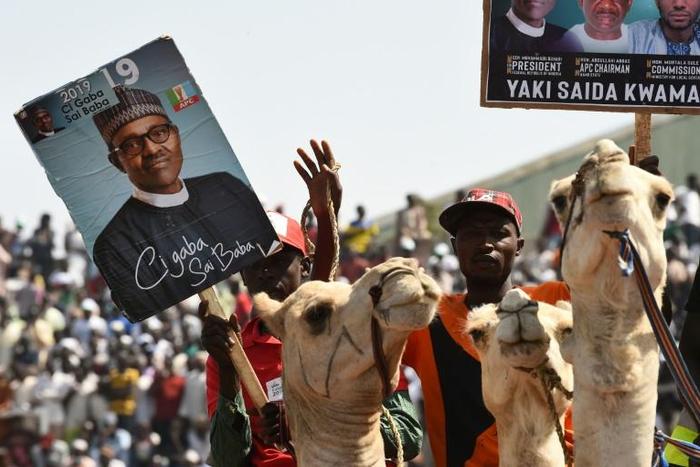 Supporters on camels hold banners of Nigeria's ruling All Progressives Congress during an election rally in Kano
