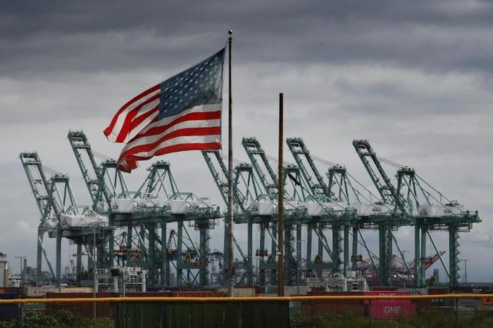 The US flag flies over shipping cranes and containers in Long Beach, California, where a lot of Chinese exports land