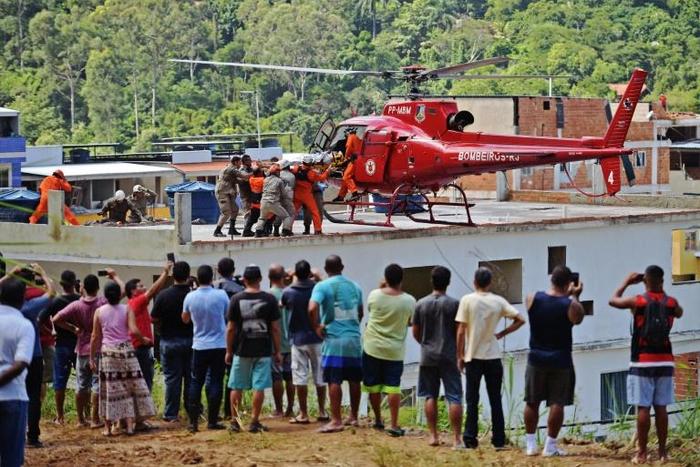 People watch as an injured person is carried onto a rescue helicopter after two buildings collapsed in Muzema, Rio de Janeiro, Brazil