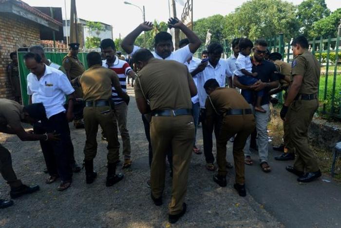 Sri Lankan policemen carry out a security check on men attending a funeral ceremony for a bomb blast victim in Colombo