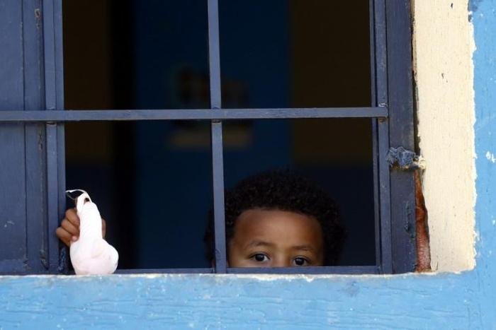 A child from a family of African migrants peeks out from a window at Libyan detention center, among thousands who have tried in recent years to flee to Europe via the North African country