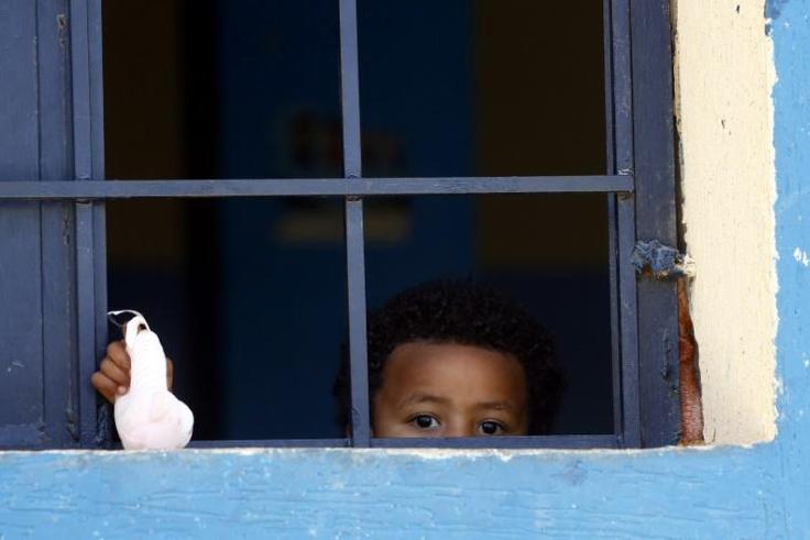 A child from a family of African migrants peeks out from a window at Libyan detention center, among thousands who have tried in recent years to flee to Europe via the North African country