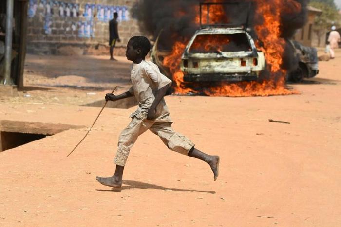 A boy runs off as cars are set on fire in Kofa
