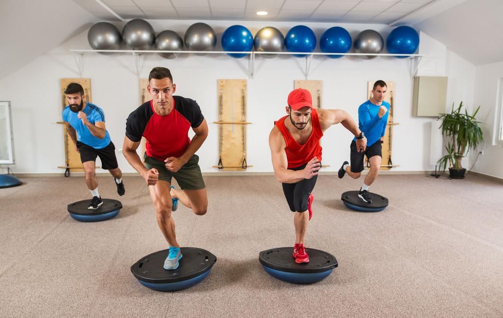 Group of men doing Pilates exercises on bosu balls.