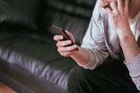 Serious bearded man is sitting on couch and typing on smartphone