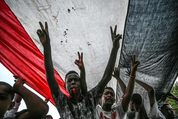 Sudanese protesters shout slogans and flash victory signs during a rally outside the army complex in Sudan's capital Khartoum