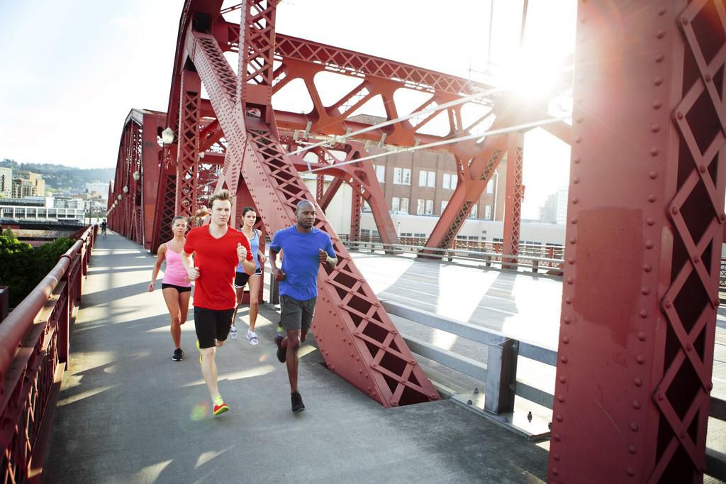 Athlete friends running on footbridge in city during sunny day