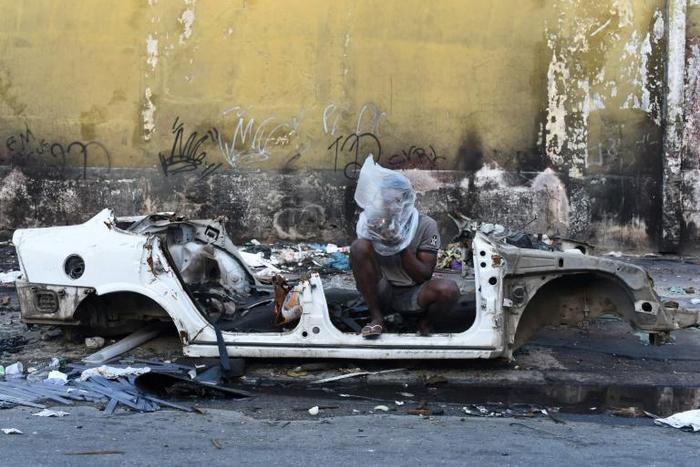 A drug user smokes crack beside the shell of a burnt out car in the Sem Terra favela in Complexo da Mare, Rio de Janeiro, on April 29, 2019