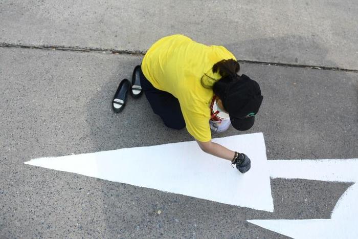 A Thailand Post employee repaints a street sign outside her office ahead of King Maha Vajiralongkorn's coronation