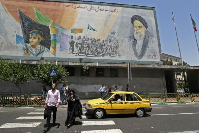Iranians walk under a mural of Ayatollah Ruhollah Khomeini, who remains a guiding figure in the country 30 years after his death
