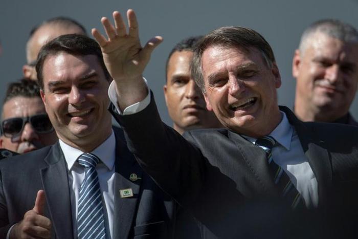 Brazilian President Jair Bolsonaro (R) waves next to his son Flavio, a federal senator who denies any impropriety after a report that he allegedly made more than three million reais ($790,000) buying and selling 19 apartments and commercial locations i...