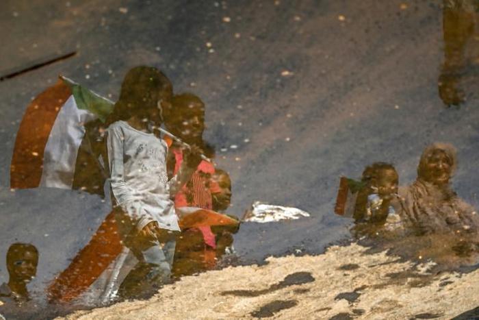 A reflection in a puddle of Sudanese protesters as they carry national flags outside the army headquarters in the capital Khartoum on Saturday