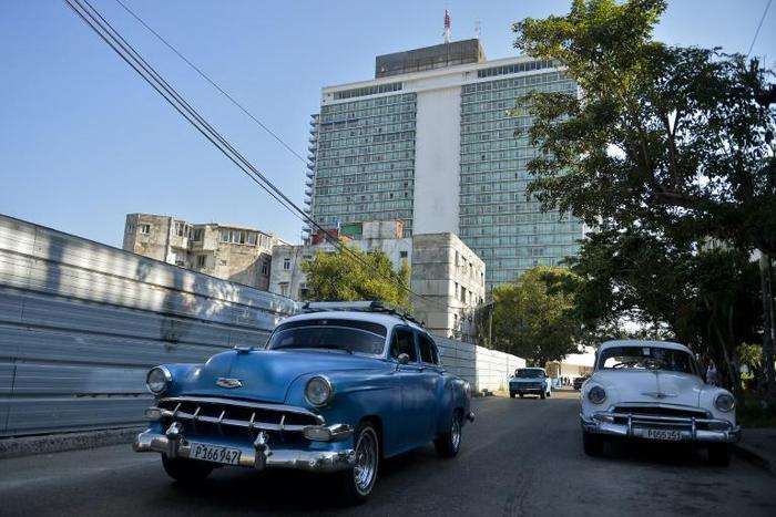 Old American cars drive near the emblematic Hotel Habana Libre, which could be affected by Title III