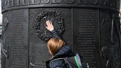 People touch the Hillsborough Memorial Monument as Liverpool observes a minute's silence on the 30th anniversary of the stadium disaster that took the lives of 96 Reds fans