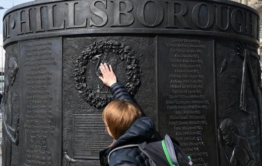 People touch the Hillsborough Memorial Monument as Liverpool observes a minute's silence on the 30th anniversary of the stadium disaster that took the lives of 96 Reds fans