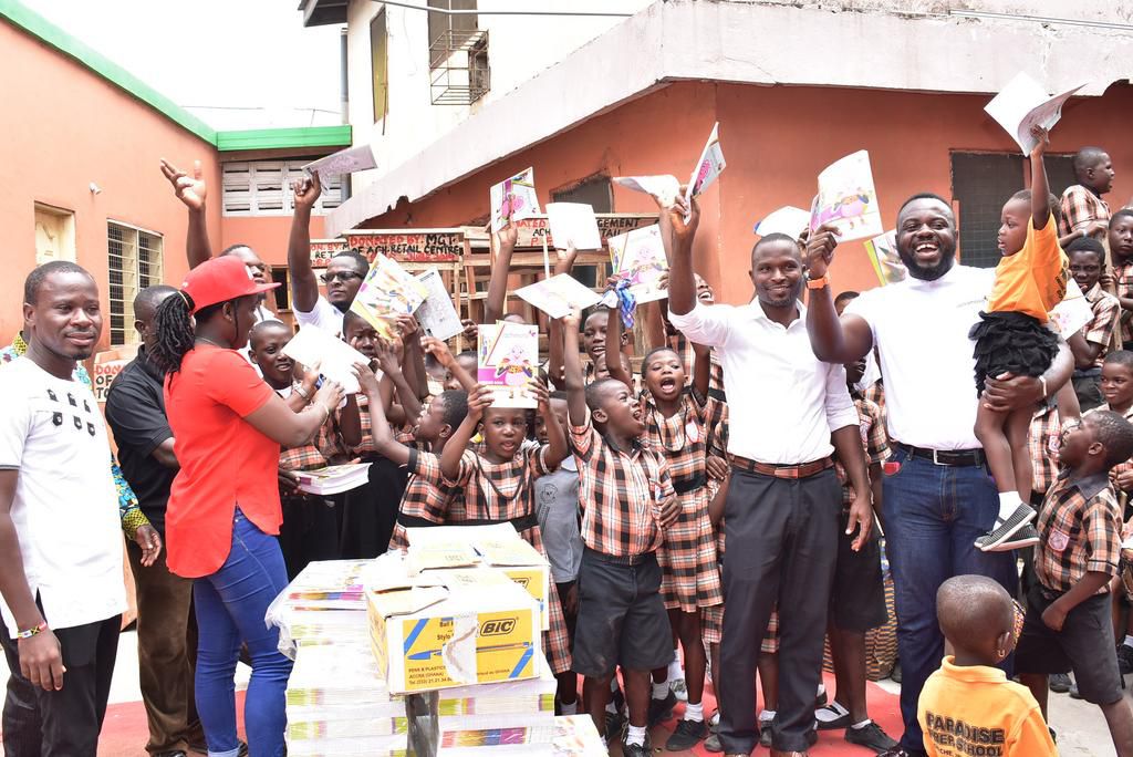 Mr. Asamoah (right, carrying a KG pupil) joins the assistant headmaster and jubilant schoolchildren to show off their new exercise books.