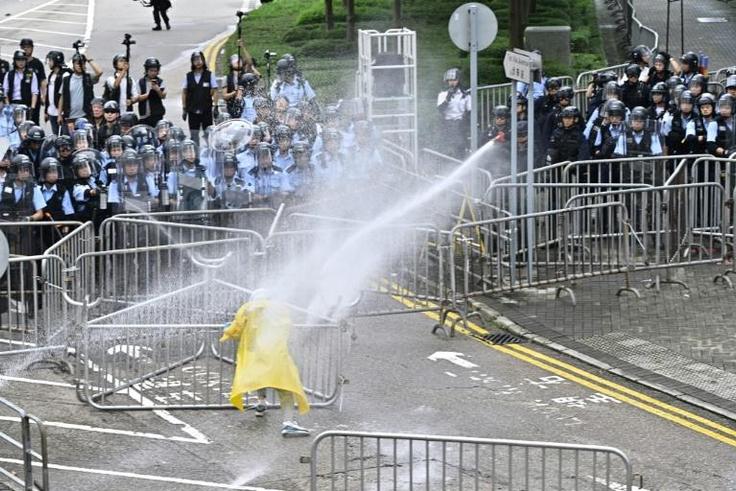 Police officers use a water canon on a lone protestor near the government headquarters in Hong Kong