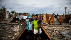Iris Daniel, 57, Lovely Saint-Pierre, 32, and Evanston Daniel, 5, pose on May 25, 2019, outside a makeshift shelter on the site of their home which was burned during a November 2018 gang war in Port-au-Prince