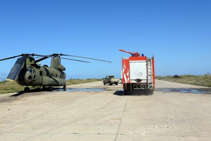In this file photo, a firefighting truck is parked next to an Italian-built Libyan Chinook CH-47 military helicopter that was hit by shrapnel following an air strike at Mitiga International Airport in early April