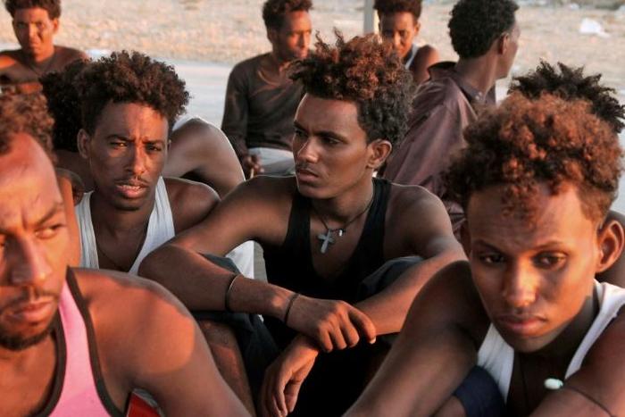Rescued migrants sit on the coast in the fishing village of Khoms, east of the Libyan capital