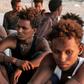 Rescued migrants sit on the coast in the fishing village of Khoms, east of the Libyan capital