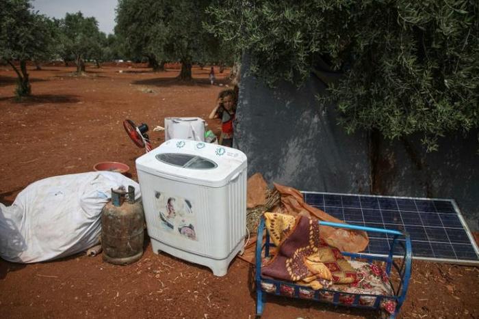A Syrian girl stands behind family belongings near a camp for displaced people in the village of Atme, northern Idlib province