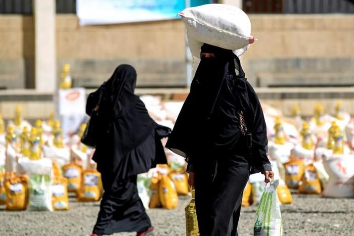 A Yemeni woman carries a sack of grain on her head while walking after receiving food aid provided by a local charity