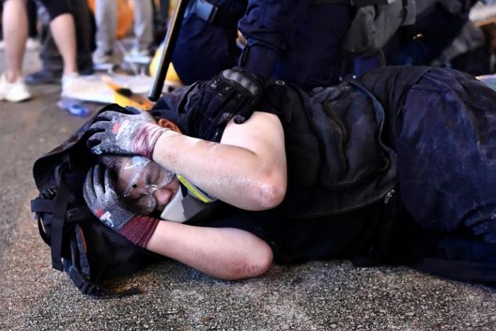 A protester is detained by police during a demonstration in Hong Kong. Police say they will charge dozens with rioting in the wake of recent violence
