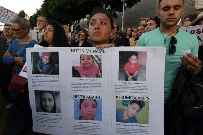 A woman holds photos of migrant children who have died in US custody as people protest in LA against the upcoming ICE raids and detentions of refugee asylum seekers
