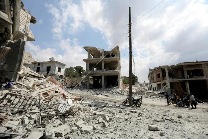 A picture taken on June 14, 2019, shows people gathering next to a damaged building in the town of Ihsim, in Syria’s Idlib region, scene of heavy bombardments by Syrian government forces and its ally Russia