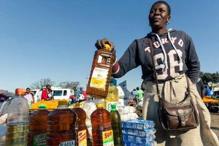 A customer buys cooking oil at a stall where smaller than standard measures of cooking oil is sold at Harare Mbare Musika marketplace as inflation sends food prices soaring