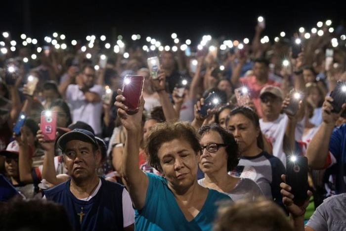 People hold up their phones during a prayer and candle vigil organized by the city, after a shooting left 20 people dead at the Cielo Vista Mall Wal-Mart in El Paso, Texas, on August 4, 2019