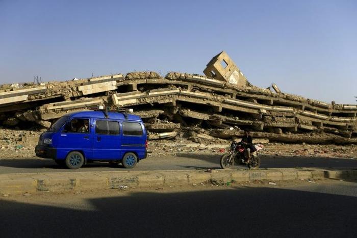 A van drives by a building flattened in Saudi-led coalition air strikes in Amran, 50 kilometres (30 miles) north of the Yemeni capital Sanaa