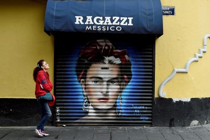 In this file picture taken on August 30, 2017 a woman walks past a mural of Mexican artist Frida Kahlo at Mesones street in Mexico City