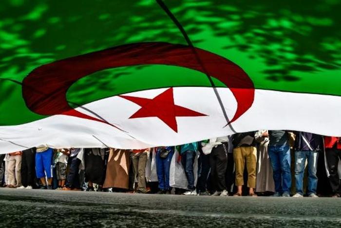 In this file photo from late May, Algerian protesters are seen from underneath a giant national flag