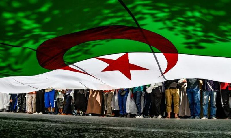 In this file photo from late May, Algerian protesters are seen from underneath a giant national flag