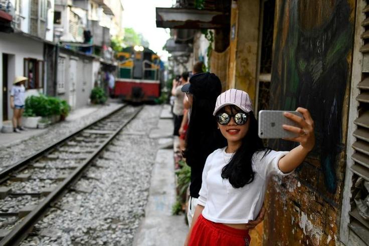 This photograph taken on June 8, 2019 shows a woman taking a selfie as a train passes in Hanoi's popular train street -- the selfie craze is universal