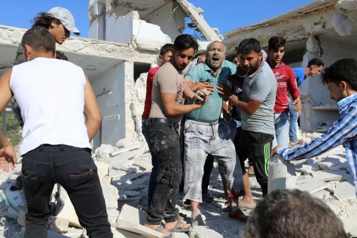 Syrian civilians help a wounded man following reported air strikes by regime forces on Maaret al-Numan in Syria's northwestern Idlib province on July 23, 2019