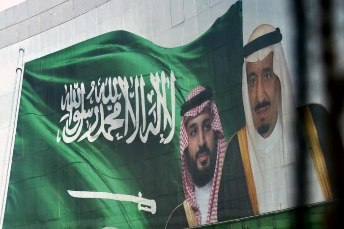 Saudi King Salman and his son Crown Prince Mohammed appear next to a Saudi flag on a billboard in Riyadh