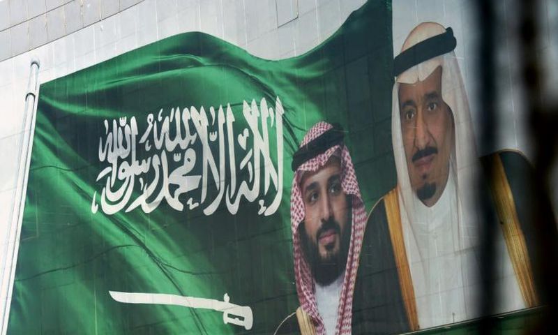 Saudi King Salman and his son Crown Prince Mohammed appear next to a Saudi flag on a billboard in Riyadh