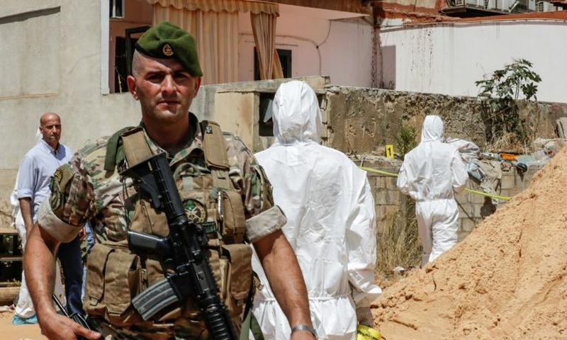 A Lebanese army soldier walks past military intelligence forensic investigators ar the scene where two drones came down in the vicinity of a media centre of the Shiite Hezbollah movement