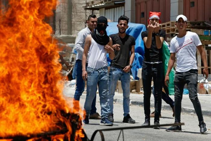 Stone-carrying Palestinians near Hebron stand behind a burning tyre as they protest against a US-led Middle East conference in Bahrain