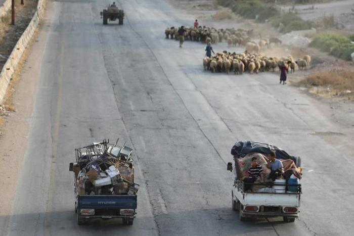 Syrian families from the southern reaches of Idlib province and the northern countryside of Hama flee in trucks loaded with their belongings