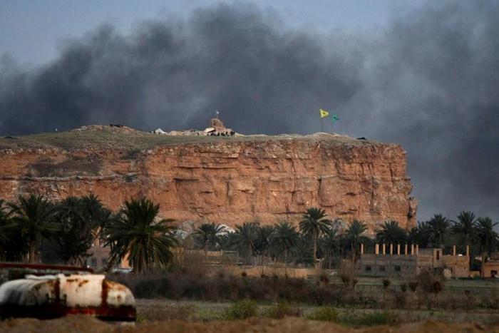 The yellow flag of the Syrian Democratic Forces flutters on a hilltop above the Islamic State group's last redoubt of Baghouz as the US-backed fighters proclaim the total elimination of its "caliphate"