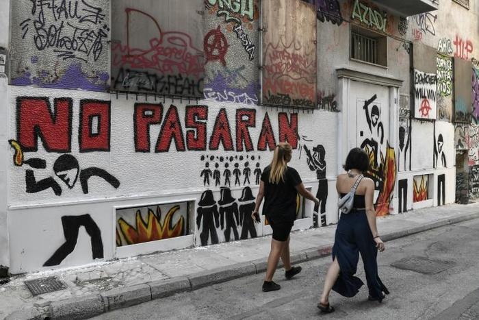 Women walk past a recent graffiti in Athens' historic district of Exarchia