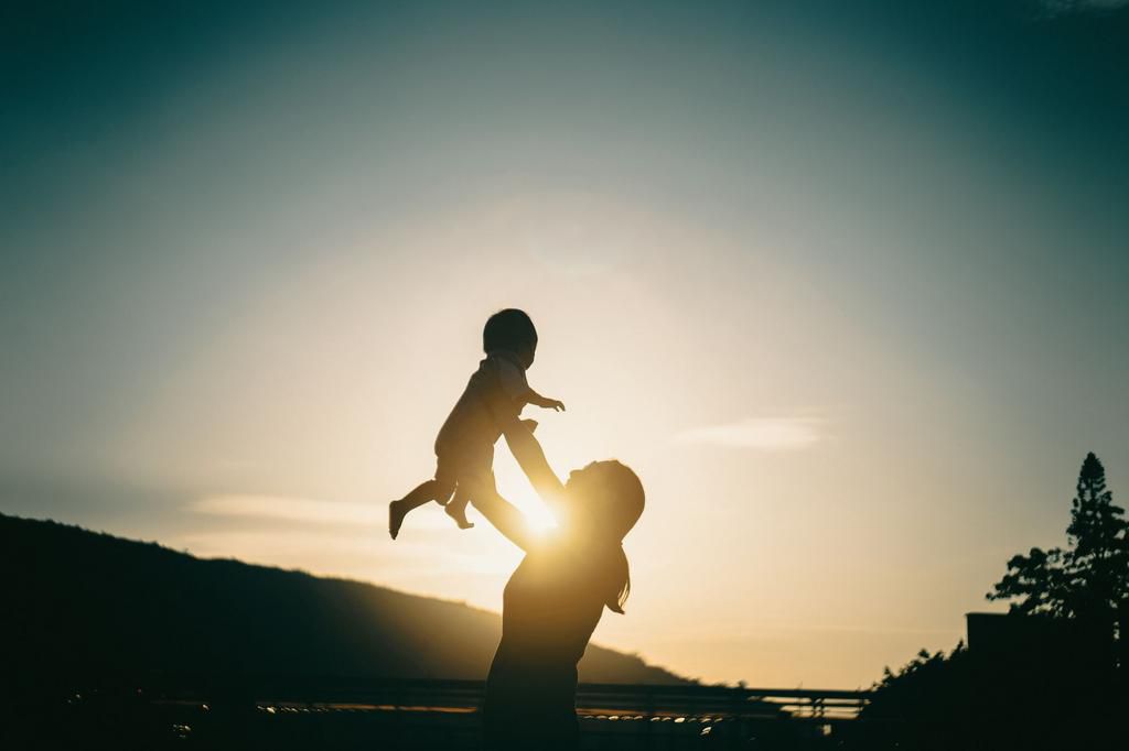 Silhouette of mother raising baby girl in the air outdoors against sky during a beautiful sunset